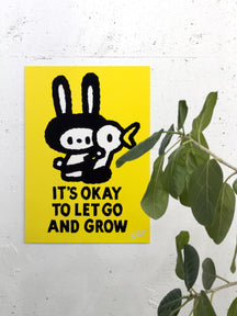IT'S OKAY TO LET GO AND GROW, TAROART by TAROUT 00030, displayed on a white wall beside a green plant